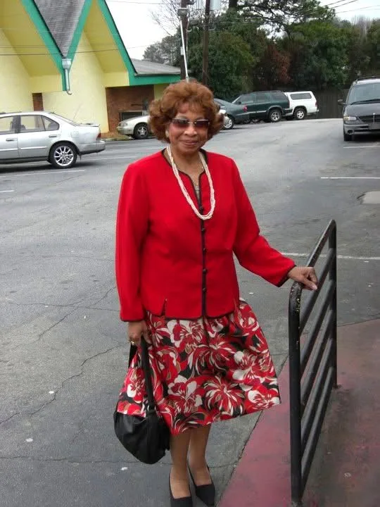 Missionary Katherine Cash Griffey standing outdoors in a red jacket and floral skirt, handbag in hand.